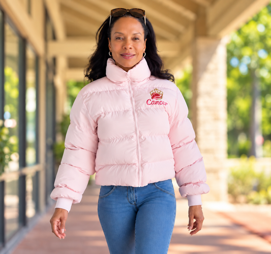 Women's pink puffer jacket. Embroidered paw logo with a pink bow around the wrist. The word cancer is under the paw. 