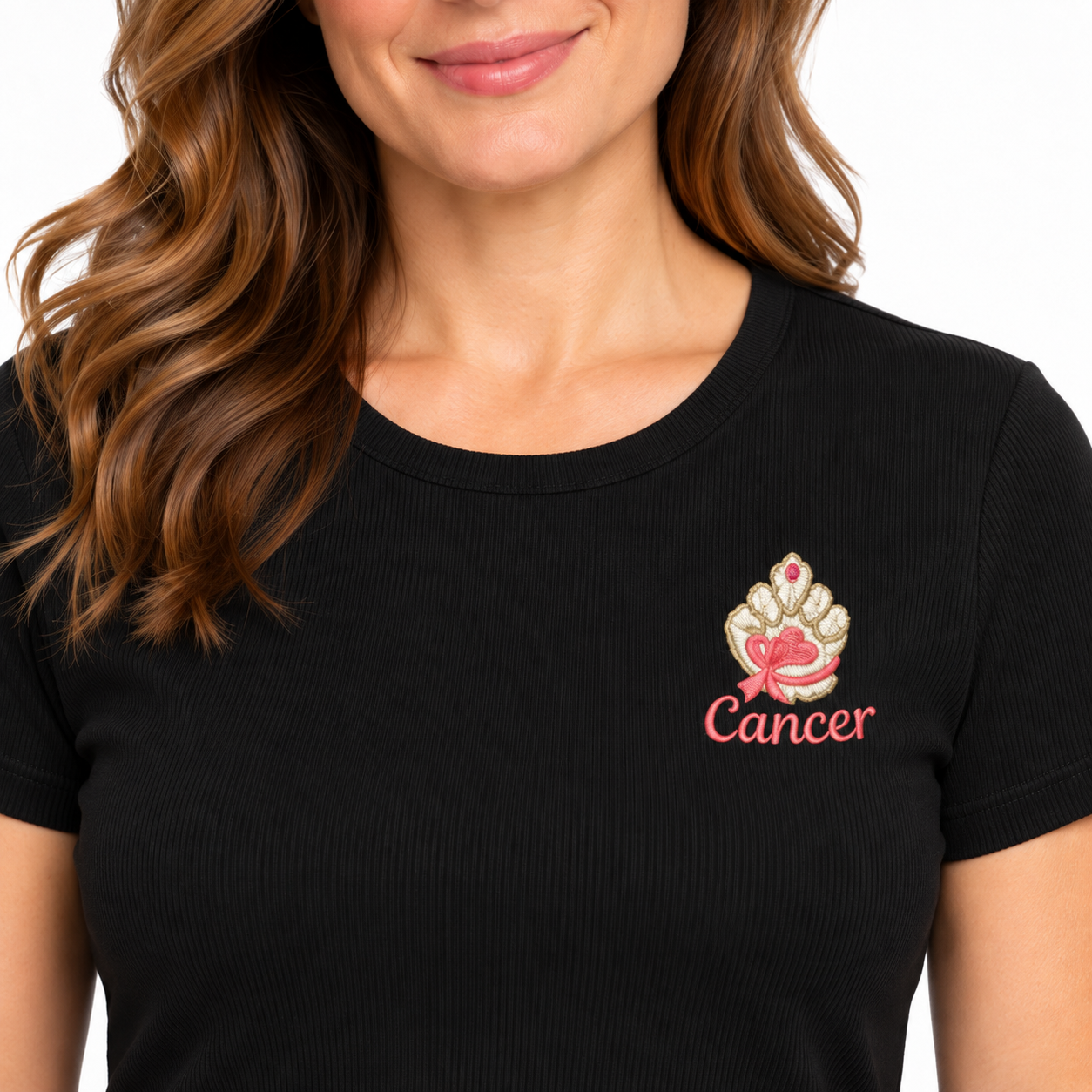 A close-up of a woman wearing a black ribbed short-sleeve t-shirt with a custom graphic on the left chest. The graphic features a gold and white crown with a pink ribbon and the word 'Cancer' in pink script.