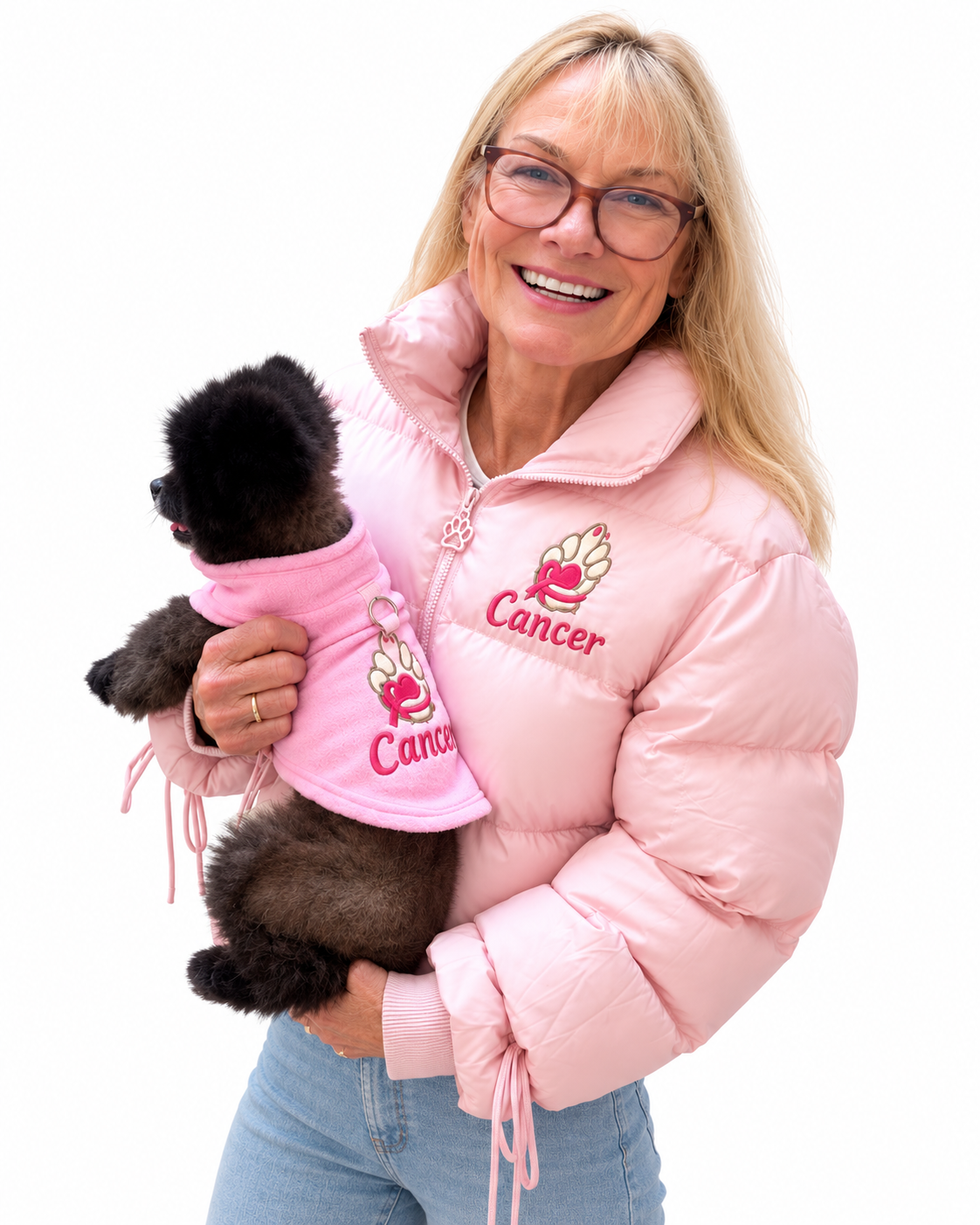Women is a pink puffer jacket with an embroidered  paw logo with the word cancer underneath the paw holding a dog with a pink fleece with an embroidered paw logo with a pink ribbon around the paw with the word cancer underneath the paw.