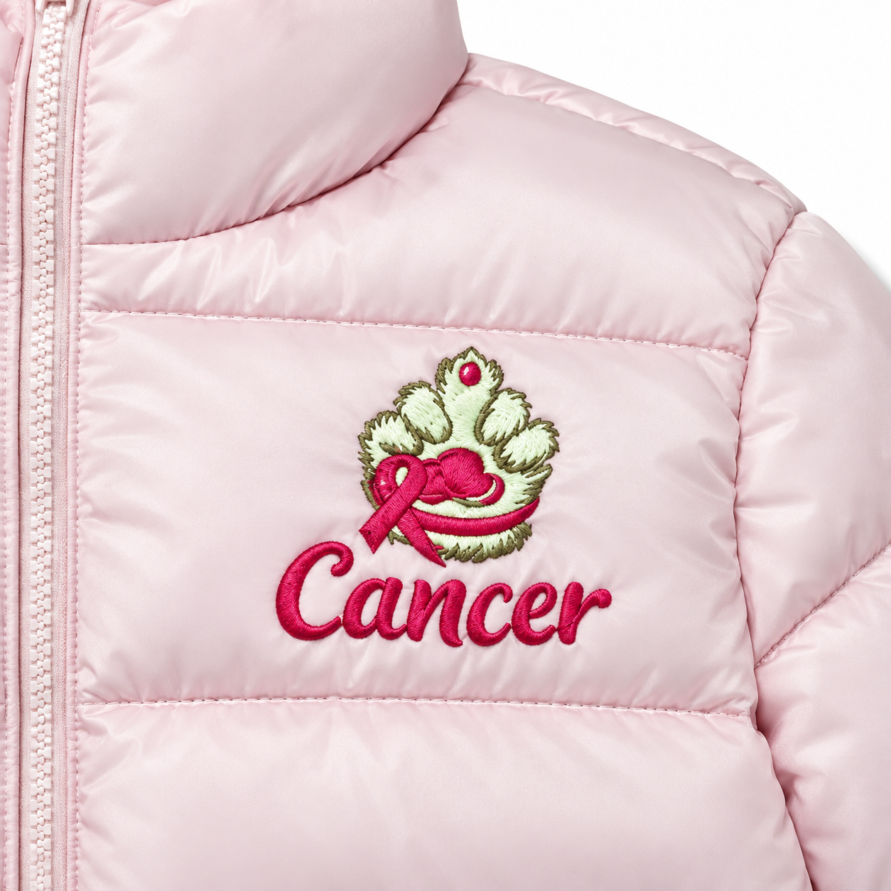 Close-up of a light pink puffer jacket with an embroidered chest graphic featuring a green wreath with a pink ribbon and the word 'Cancer' in pink script.