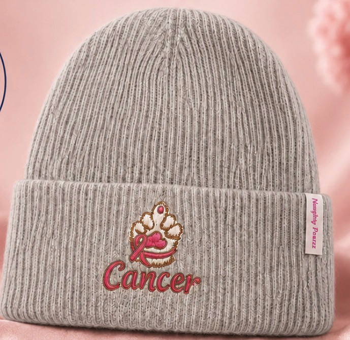 A light gray ribbed knit beanie hat with a cuffed brim, featuring an embroidered pink and gold crown with a pink ribbon and the word 'Cancer' in red. A small side tag reads 'Memphis Purple'.