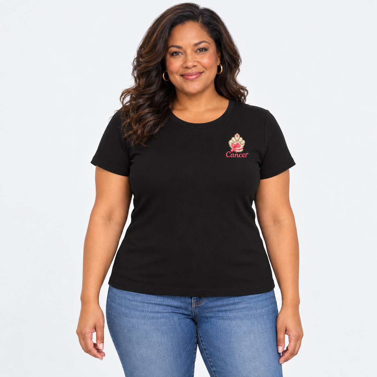 A woman modeling a black short-sleeve crewneck t-shirt with a small pink and white 'Cancer' paw print graphic on the left chest, paired with blue jeans against a light gray background.