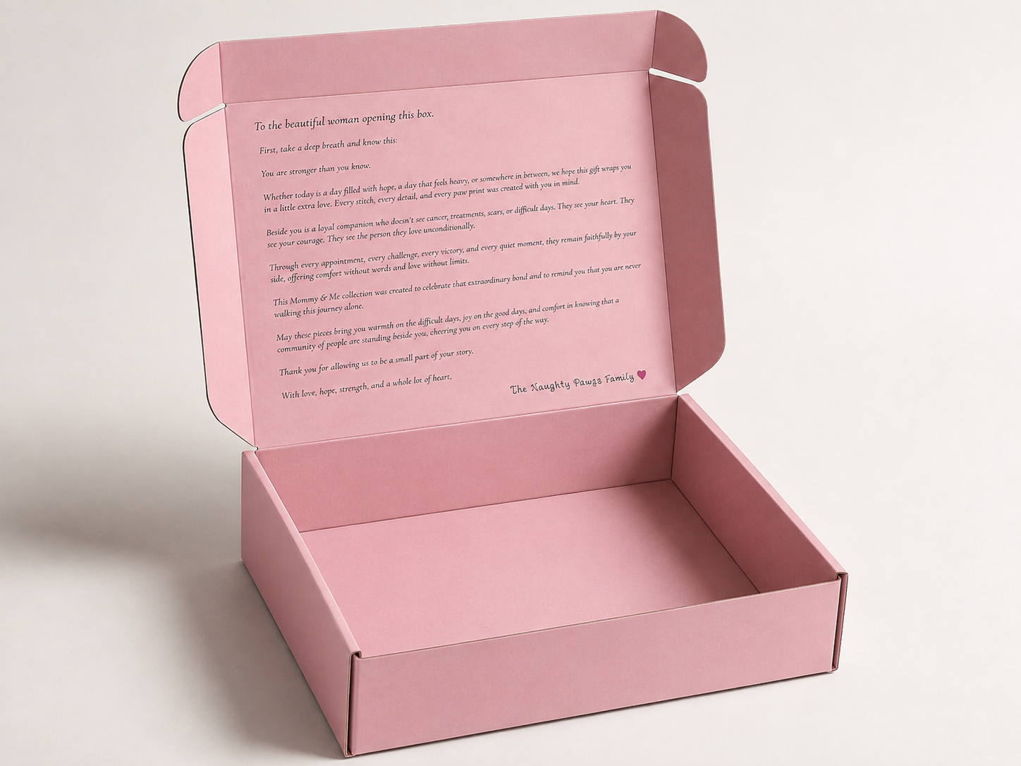 An open pink cardboard gift box with a printed message on the inside lid, photographed on a clean light gray background.