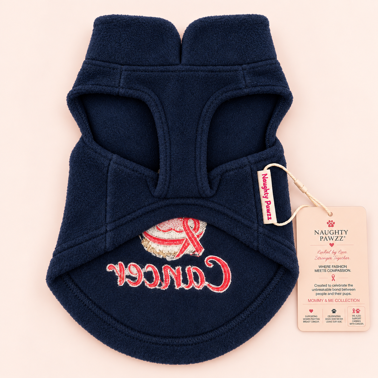 A navy blue fleece pet sweater from the back side of the fleece with an embroidered design featuring a gold and red paw print with a red ribbon and the word 'Cancer' in red script. Detailed with Naughty Pawzz logo and hang tags.